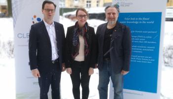 Three project people standing and smiling in front of two stands.